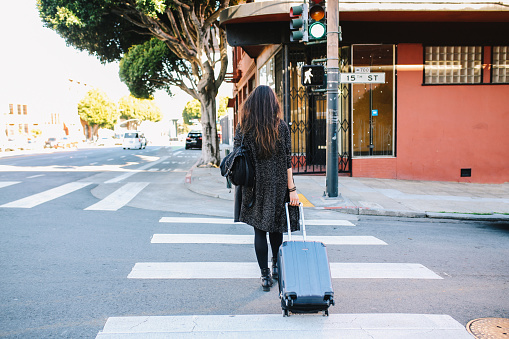 Young woman on the streets of San Francisco, California, carrying a suitcase, going to her accommodation or the travel station.