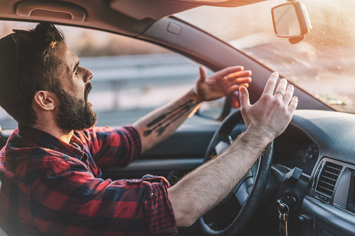 Side view image of irritated young man shouting at other drivers while driving on the highway