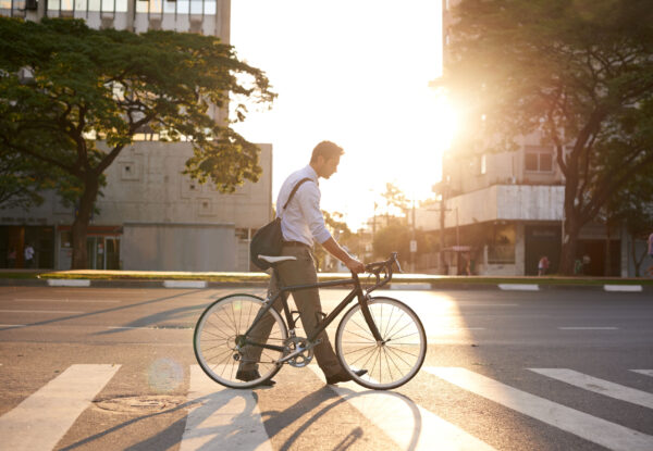 A pedestrian walking his bike across a crosswalk on his commute.