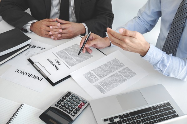 Two insurance adjusters reviewing claim documents at a desk with a laptop and calculator.