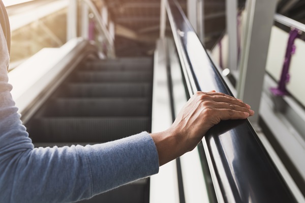 A person's hand resting on the black handrail of a moving escalator in a modern building.