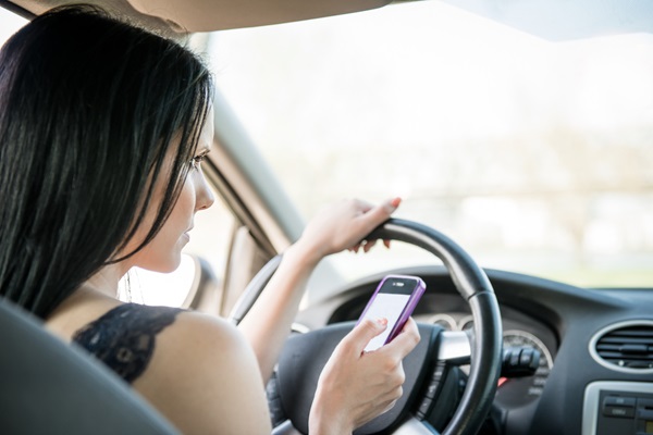 A female driver looking down at a smartphone while behind the wheel, a behavior targeted during California's CHP distracted driving enforcement campaigns throughout the month of April 2026.